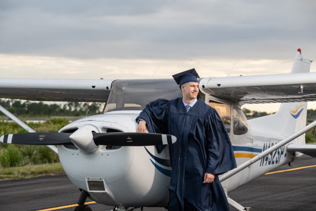 High school senior in cap and gown posing with an airplane for his graduation portraits