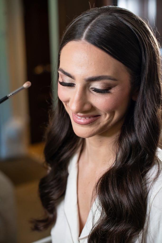 Bride smiling while having her makeup done before the wedding