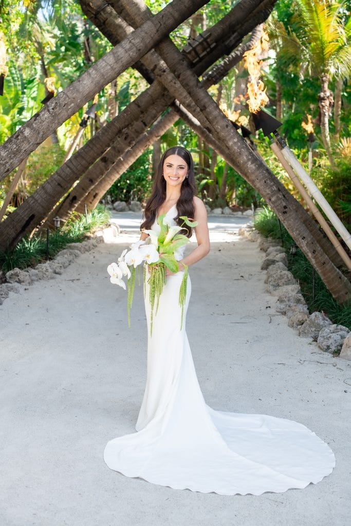 Bride holding her tropical bouquet beneath palm trees