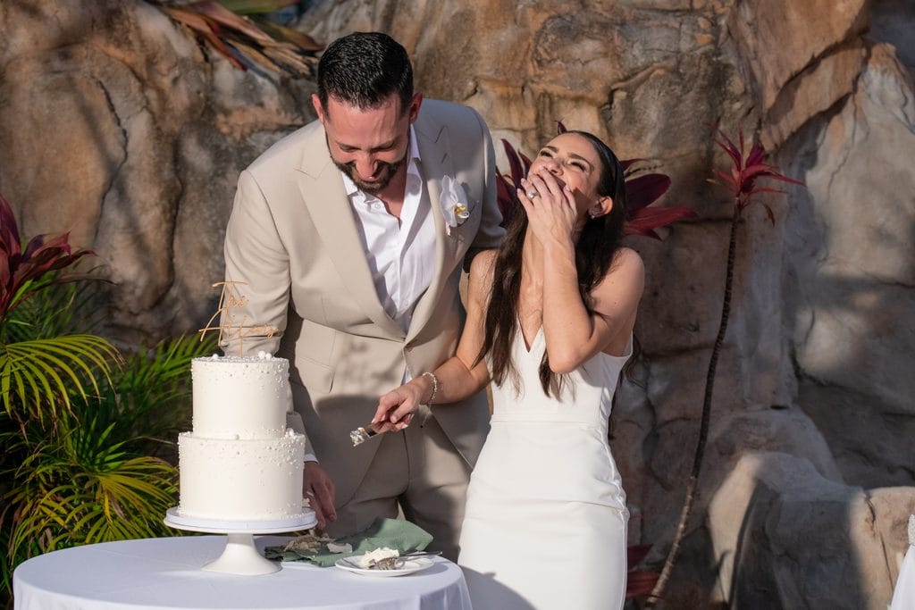 Bride laughing with groom while cutting their wedding cake