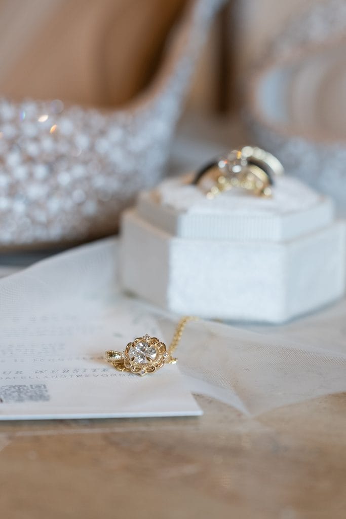 Gold pendant necklace with a clear center stone resting on sheer white fabric beside a white jewelry box.