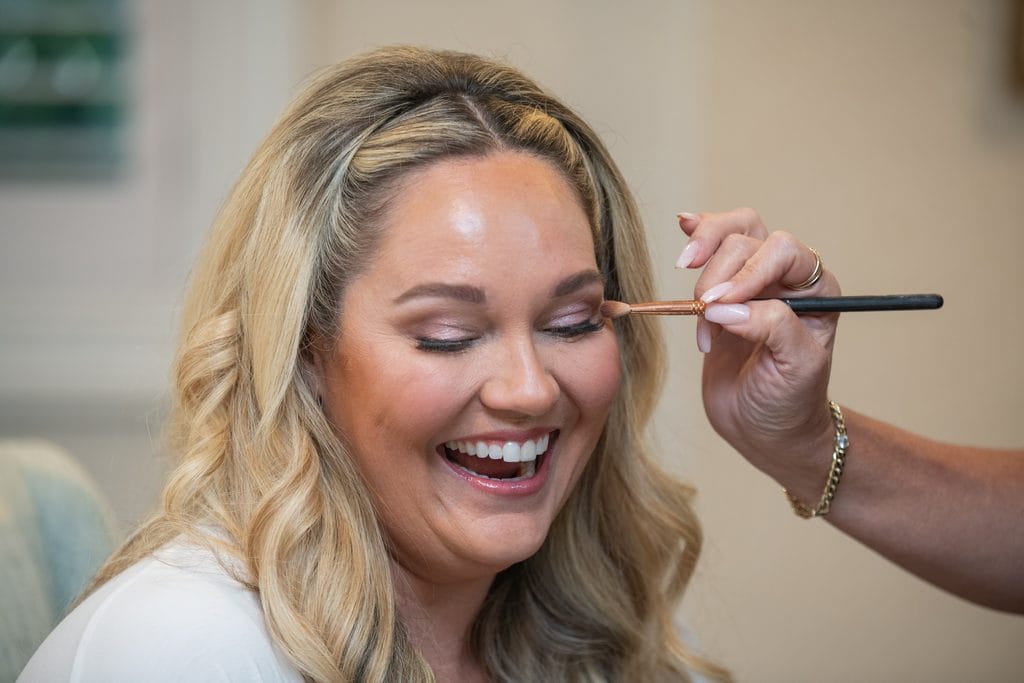 Amanda laughing as her makeup artist applies eye makeup before the wedding.