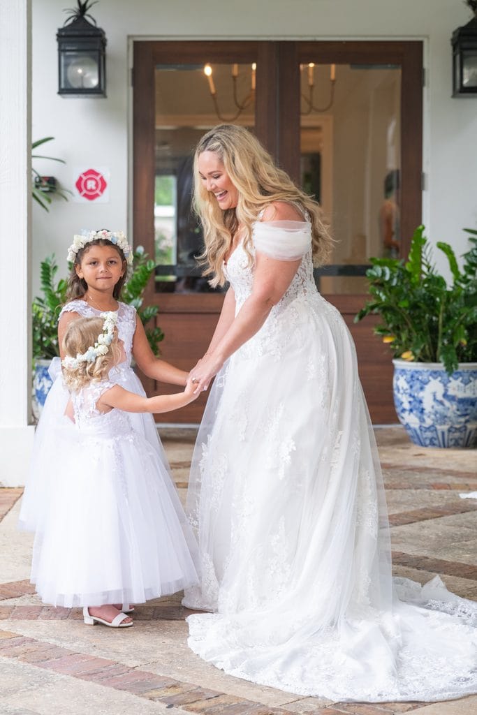 Amanda smiling and holding hands with two flower girls wearing white dresses and floral crowns 