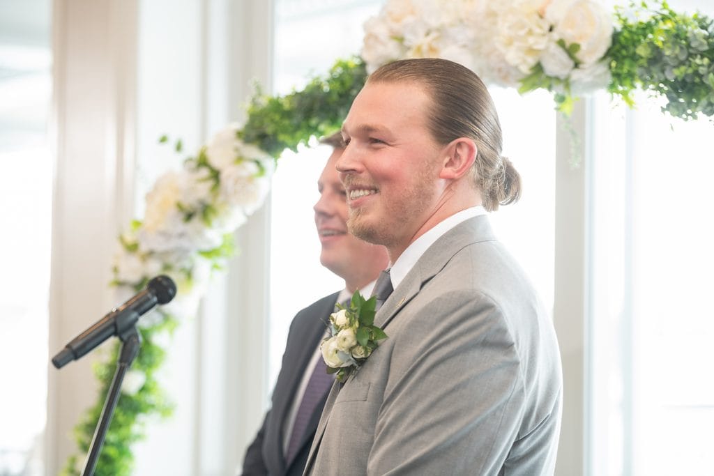 Trevor smiling as he watches Amanda walk down the aisle during their Pelican Club wedding ceremony.