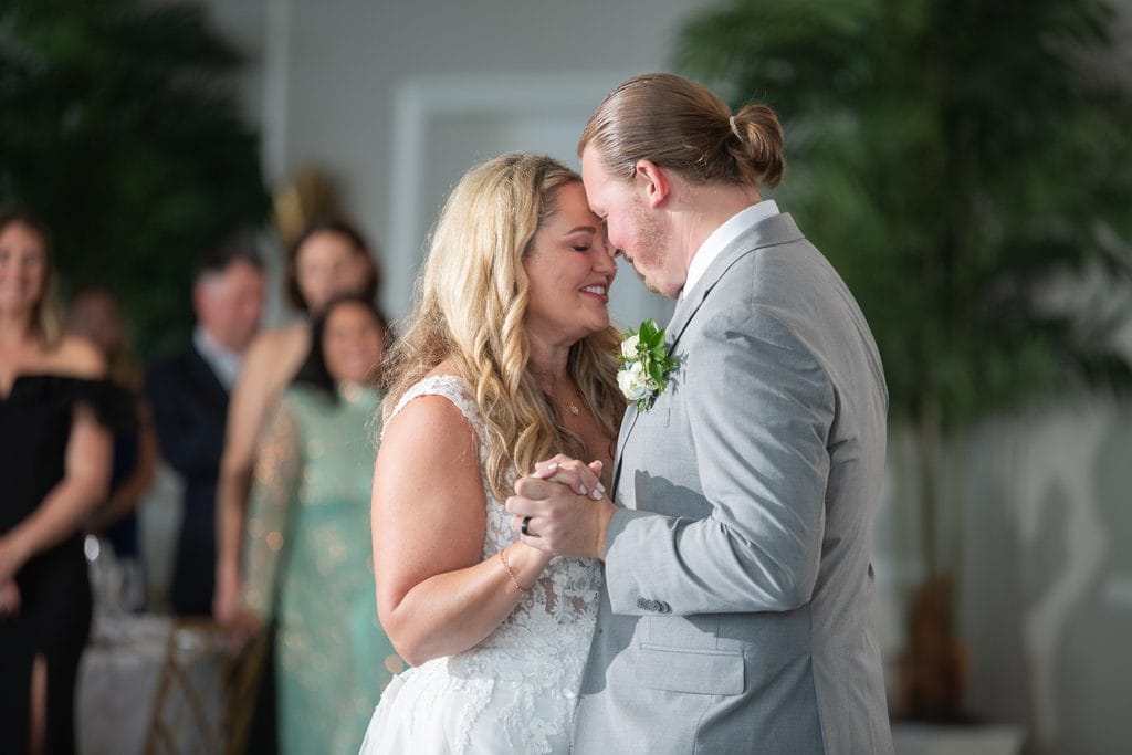 Amanda and Trevor touching foreheads and holding hands during their first dance as guest watch.