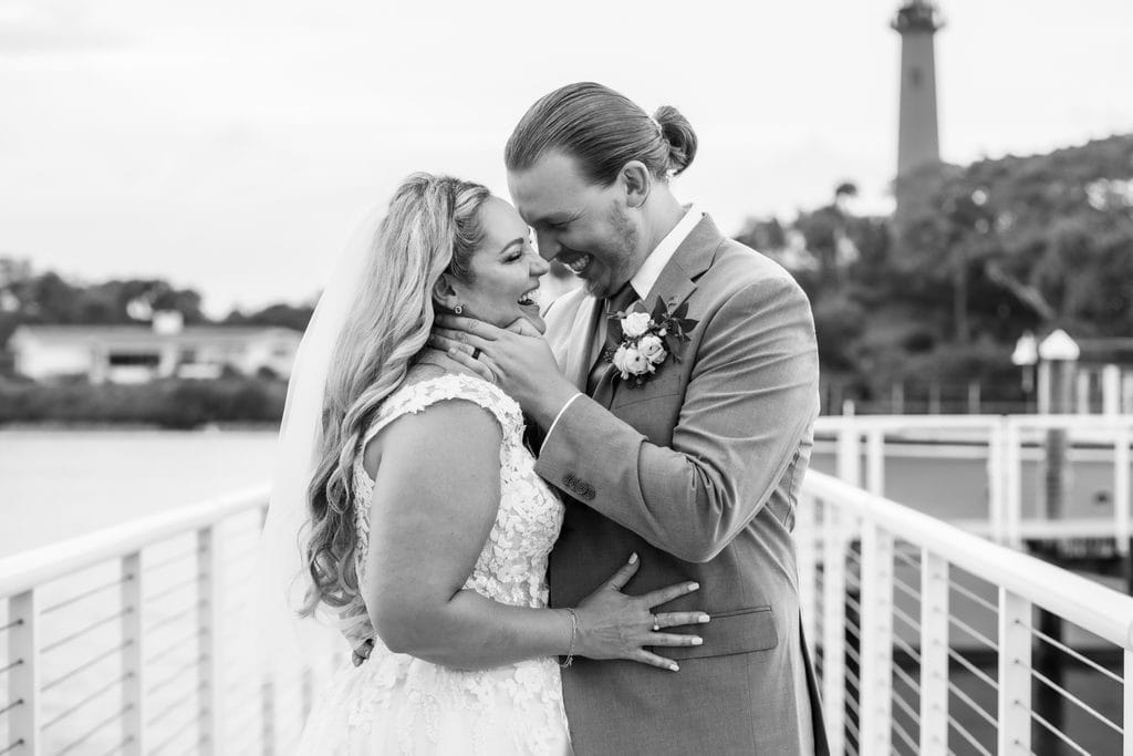 Black and white portrait of Amanda and Trevor laughing together on the waterfront walkway, with the Jupiter Lighthouse behind them.