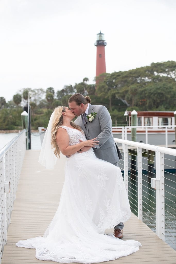 Amanda and Trevor embracing on the Pelican Club waterfront walkway with the Jupiter Lighthouse in the background.