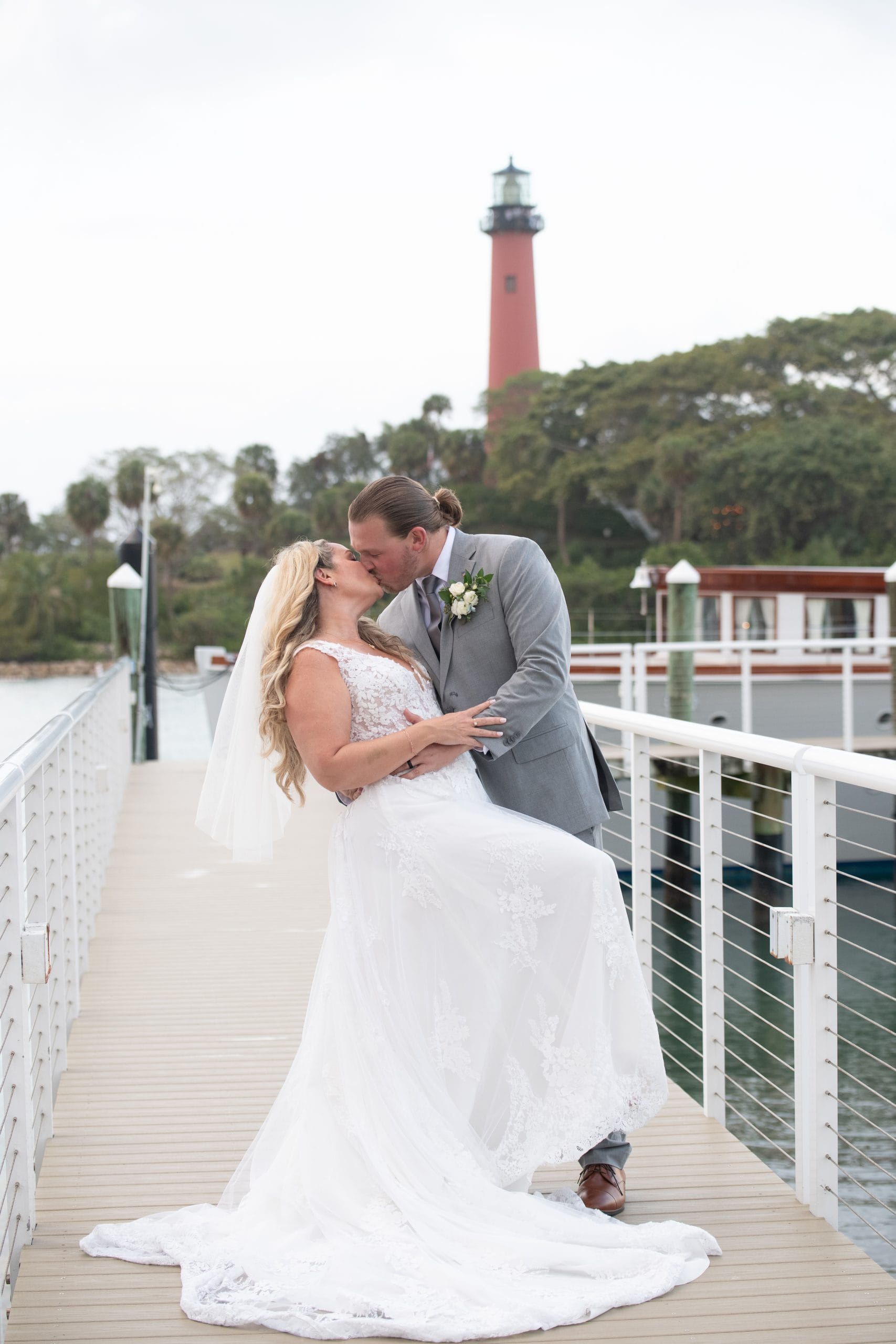 Amanda and Trevor embracing on the Pelican Club waterfront walkway with the Jupiter Lighthouse in the background.