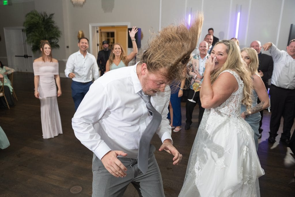 Trevor tossing his long hair while dancing as Amanda laughs and wedding guests cheer around them.